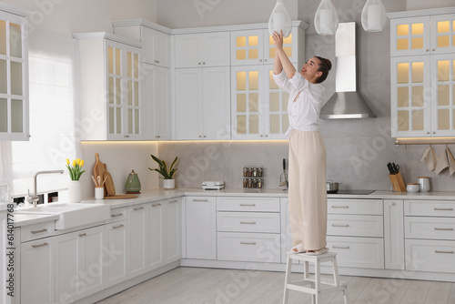 Woman on ladder changing lightbulb in ceiling lamp at home