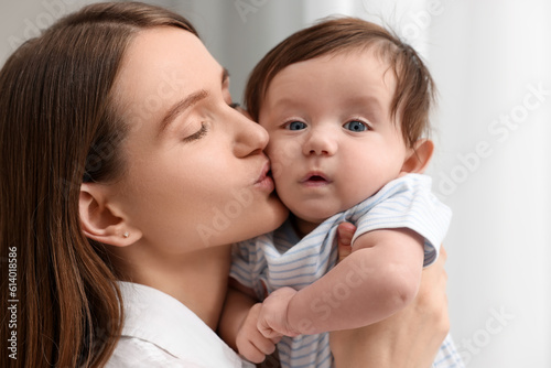 Happy mother kissing her little baby indoors, closeup