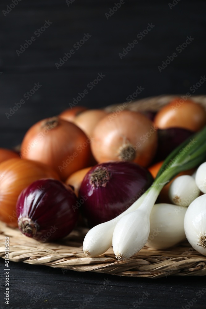 Wicker mat with different kinds of onions on black wooden table, closeup Wicker mat with different kinds of onions on black wooden table, closeup