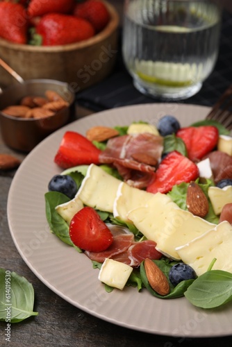 Tasty salad with brie cheese, prosciutto, almonds and berries on table, closeup