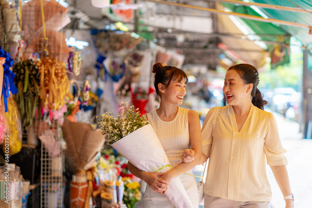 Happy Asian family mother and daughter holding flower bouquet walking together during shopping at florist shop street market in the city for flowers vase arrangement on spring summer holiday vacation.
