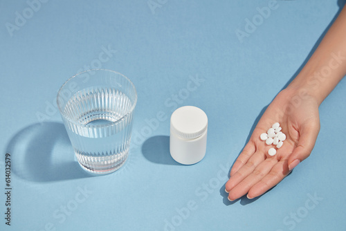 A glass of water, an unlabeled medicine bottle and a handful of pills is arranged in one line on blue background. Medicine, treatments and healthcare