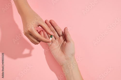 A woman hand giving a green-white capsule to a man hand over the pink background. Medicines are safe and effective