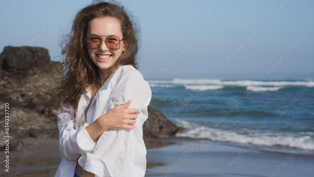 Portrait of a wealthy young woman in a white shirt and blue bikini, standing on the Bali coast of the ocean on a sunny day against the blue sky, smiling and looking. Traveling in the southern Asia. Portrait of a wealthy young woman in a white shirt and blue bikini, standing on the Bali coast of the ocean on a sunny day against the blue sky, smiling and looking. Traveling in the southern Asia.