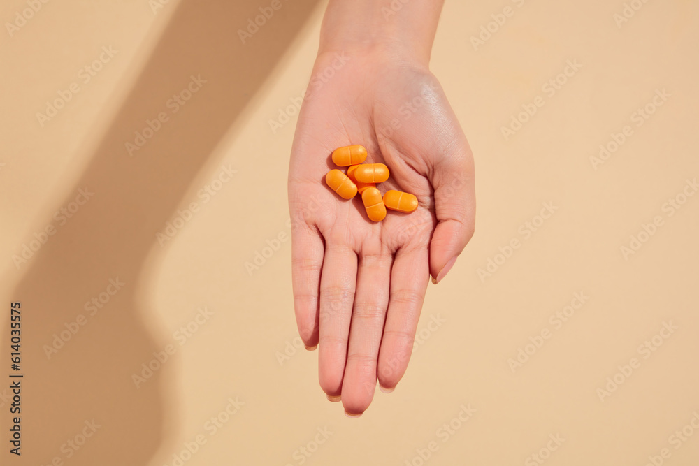 Minimal scene of a hand featuring some orange pills on a beige background. Concept of medicine and health support Minimal scene of a hand featuring some orange pills on a beige background. Concept of medicine and health support