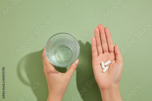 A glass of water is held in the left hand and several white pills placed on the right hand. Medication and prescription pills concept photo