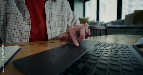 A woman in everyday ojeda uses a laptop while sitting at a table. She runs her finger over the touchpad, a close-up of a woman's hand photo