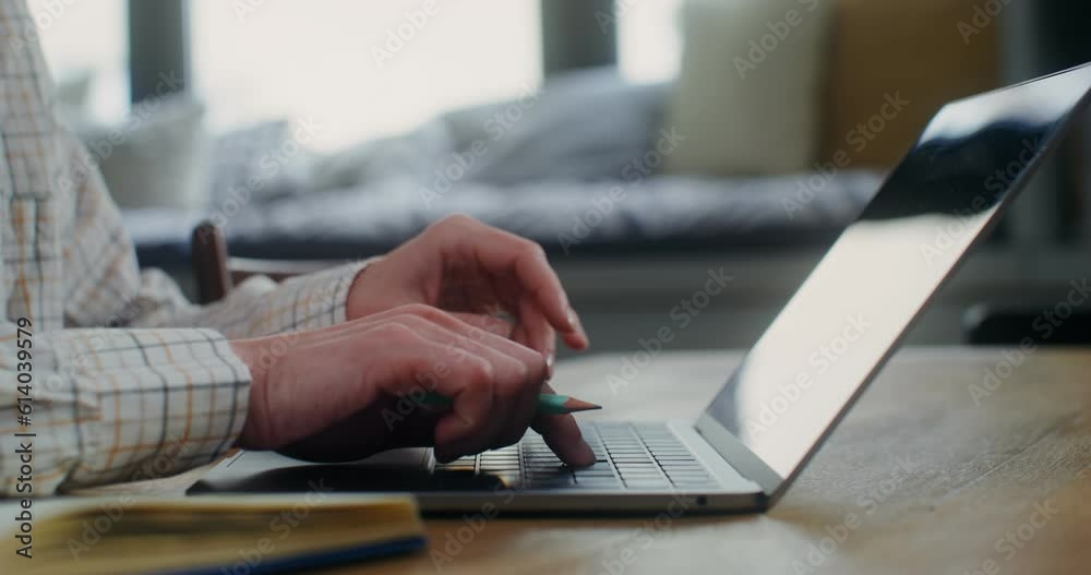A woman in casual clothes is typing on a laptop keyboard while sitting at a table in a home interior, a close-up of a woman's hands, no face