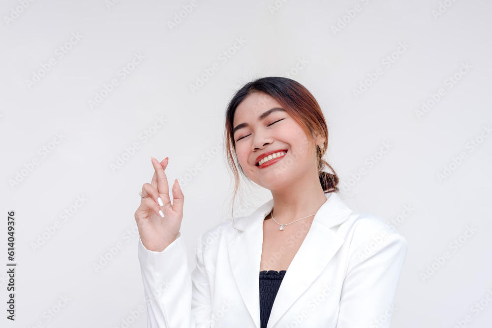 A positive and optimistic young woman holding one hand up with fingers crossed. Isolated on a white background. A positive and optimistic young woman holding one hand up with fingers crossed. Isolated on a white background.