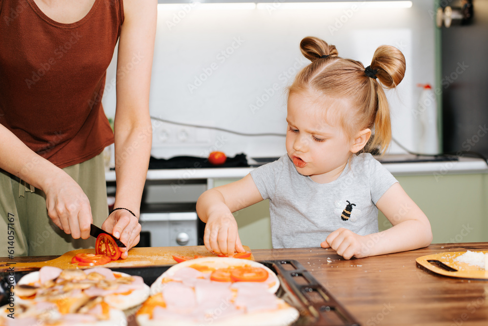 Family mom and daughter cooking pizza together, funny little cute girl child helping mom in kitchen