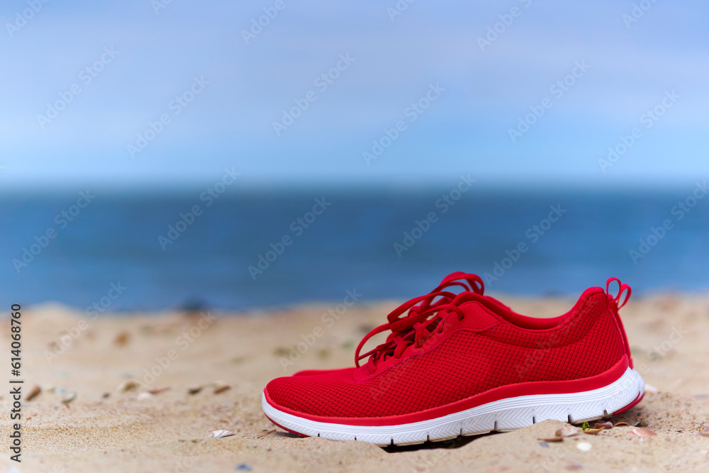 Naklejka premium Red ladies shoes on empty sandy beach. Footwear for sport and leisure on the sea. Close up.