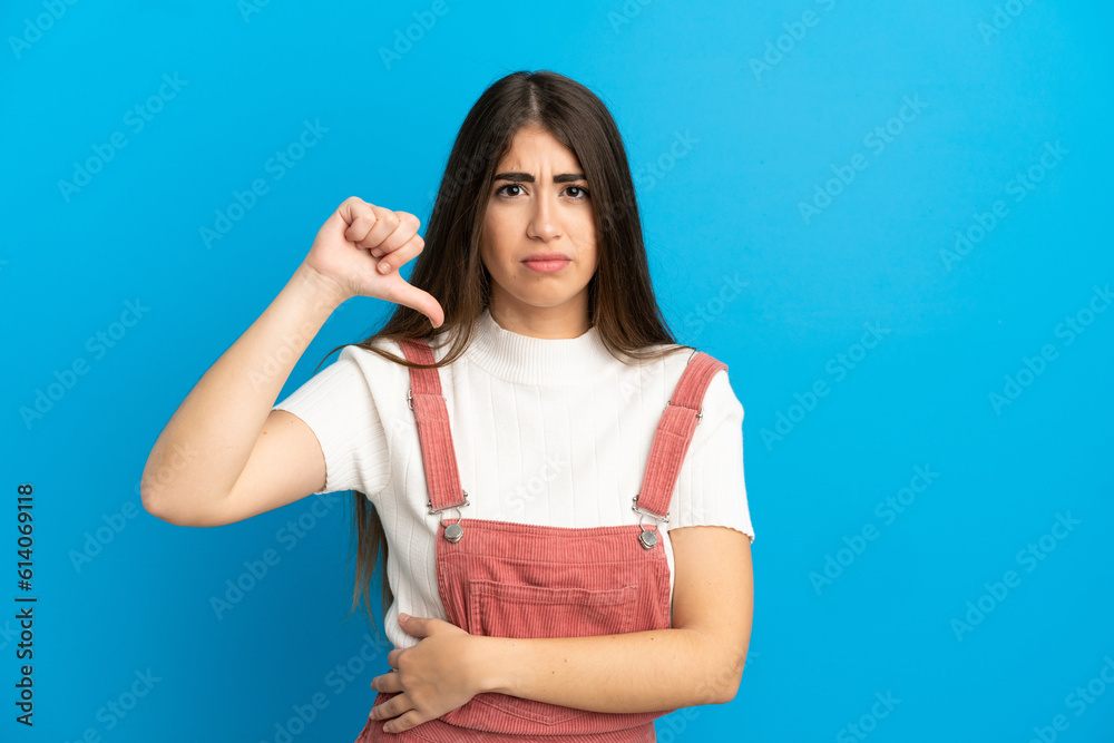 Young caucasian woman isolated on blue background showing thumb down with negative expression Young caucasian woman isolated on blue background showing thumb down with negative expression