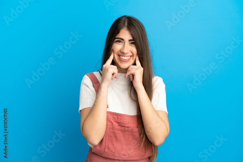 Young caucasian woman isolated on blue background smiling with a happy and pleasant expression