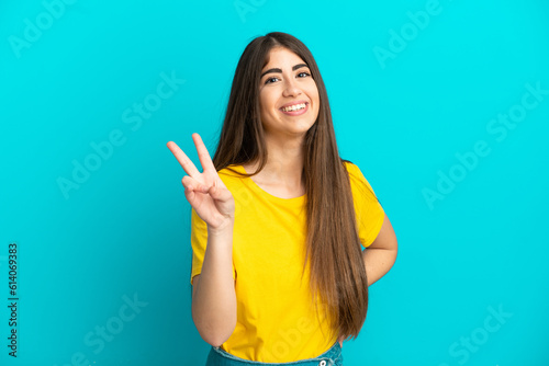 Young caucasian woman isolated on blue background smiling and showing victory sign