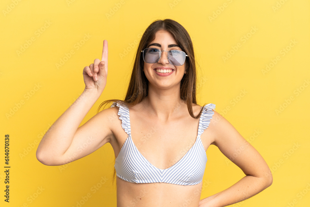 Young caucasian woman in swimsuit in summer holidays isolated on yellow background pointing up a great idea