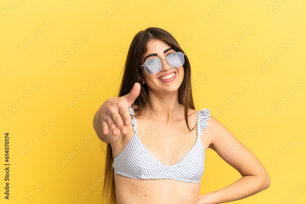 Young caucasian woman in swimsuit in summer holidays isolated on yellow background shaking hands for closing a good deal Young caucasian woman in swimsuit in summer holidays isolated on yellow background shaking hands for closing a good deal