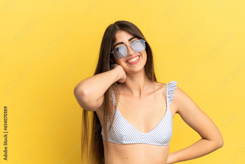 Young caucasian woman in swimsuit in summer holidays isolated on yellow background laughing