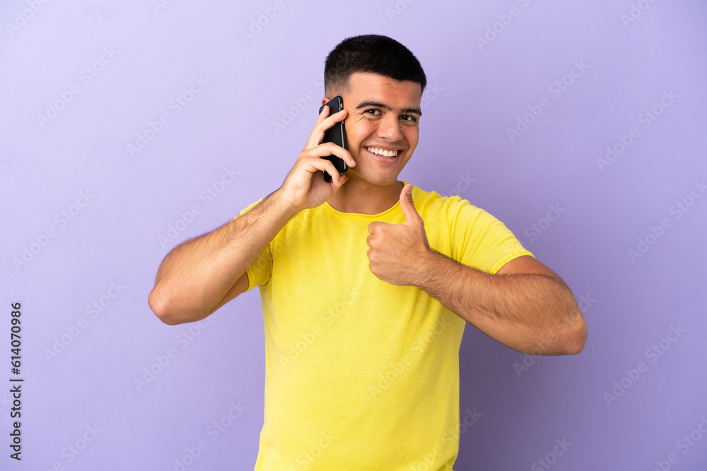 Young handsome man using mobile phone over isolated purple background giving a thumbs up gesture Young handsome man using mobile phone over isolated purple background giving a thumbs up gesture