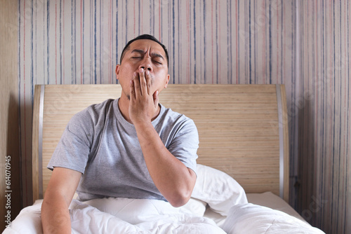 Portrait of lazy man yawning after woke up sitting on bed