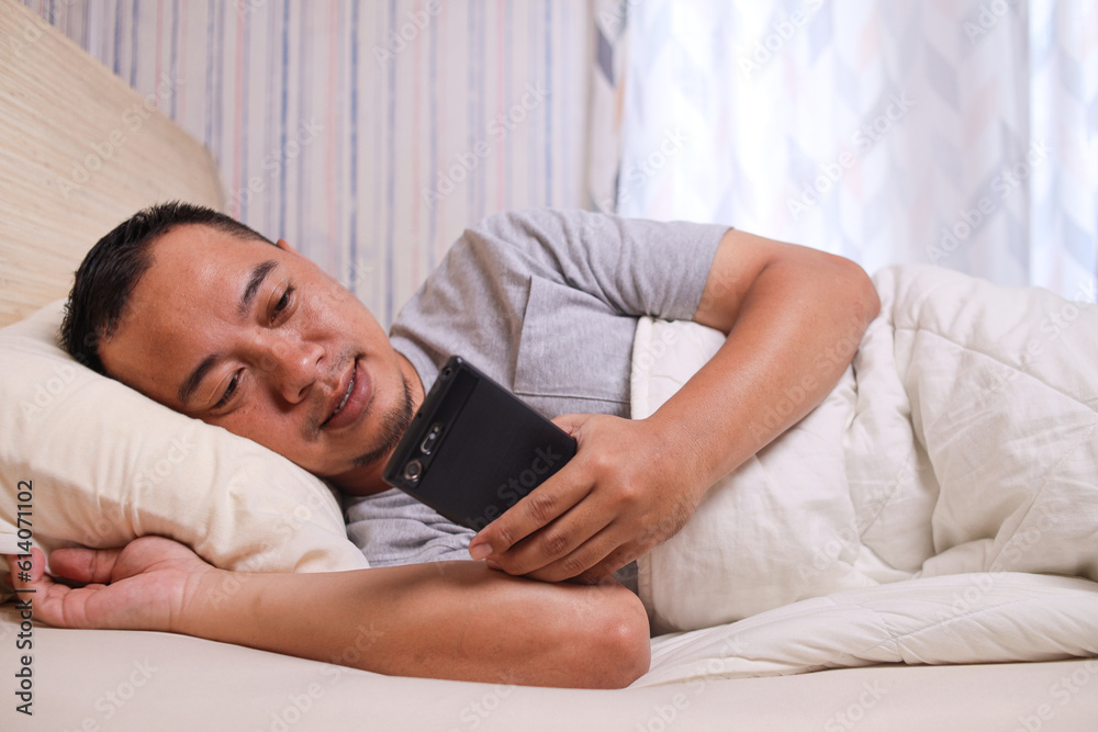 Insomnia men using smartphone while lying on the bed using a blanket Insomnia men using smartphone while lying on the bed using a blanket