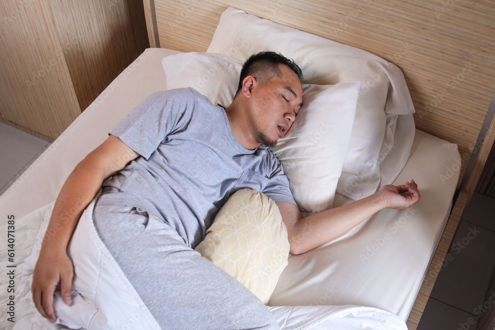 Young Asian man sleeping and snoring loudly lying in the bed