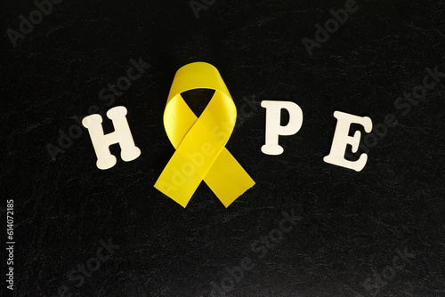 Yellow cancer awareness ribbon color with word hope on dark black background. Bone cancer awareness and suicide prevention concept.