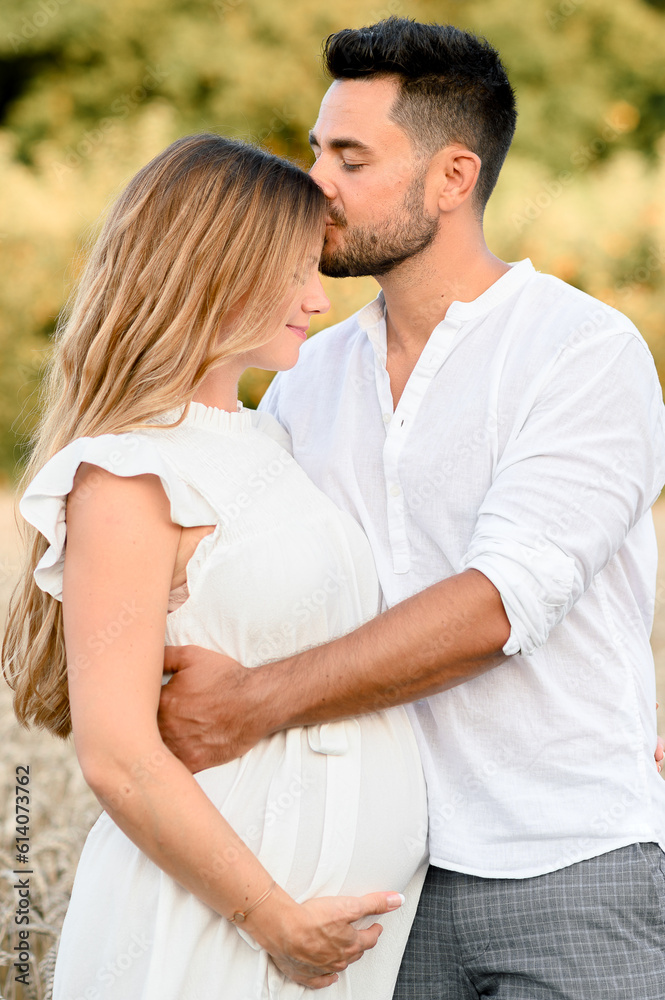 Happy husband with pregnant wife hugging and kissing in field