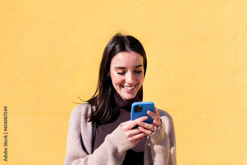 smiling young woman using mobile phone in a yellow background, concept of technology of communication and modern lifestyle, copy space for text smiling young woman using mobile phone in a yellow background, concept of technology of communication and modern lifestyle, copy space for text