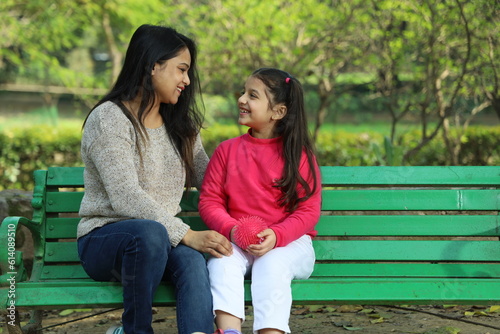 Happy Indian mother and daughter having a good time in park surrounded with lush green area.