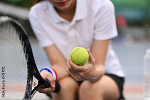 Select focus on hands of female tennis player holding ball racket sitting on the bench at tennis court. Sport, training and active life