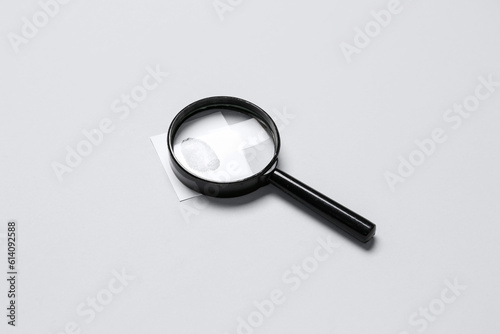 Magnifier and paper with fingerprint on grey background. Detective concept
