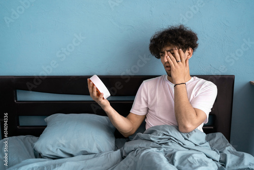 Young man overslept with alarm clock in bed in the morning. Being late concept