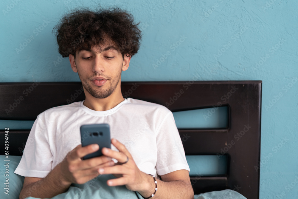 Fototapeta premium Handsome man, bed and phone in home bedroom for social media, internet browsing in the morning. Technology, relax and networking at home