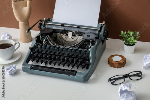 Vintage typewriter with cup of coffee, wooden hand and eyeglasses on white table near brown wall