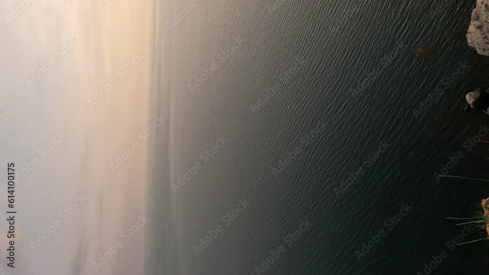 A red burning sunset with the silhouette of a cliff over sea. Abstract nature summer or spring ocean sea background. Small waves on golden warm water surface with bokeh lights from sun. Vertical video A red burning sunset with the silhouette of a cliff over sea. Abstract nature summer or spring ocean sea background. Small waves on golden warm water surface with bokeh lights from sun. Vertical video