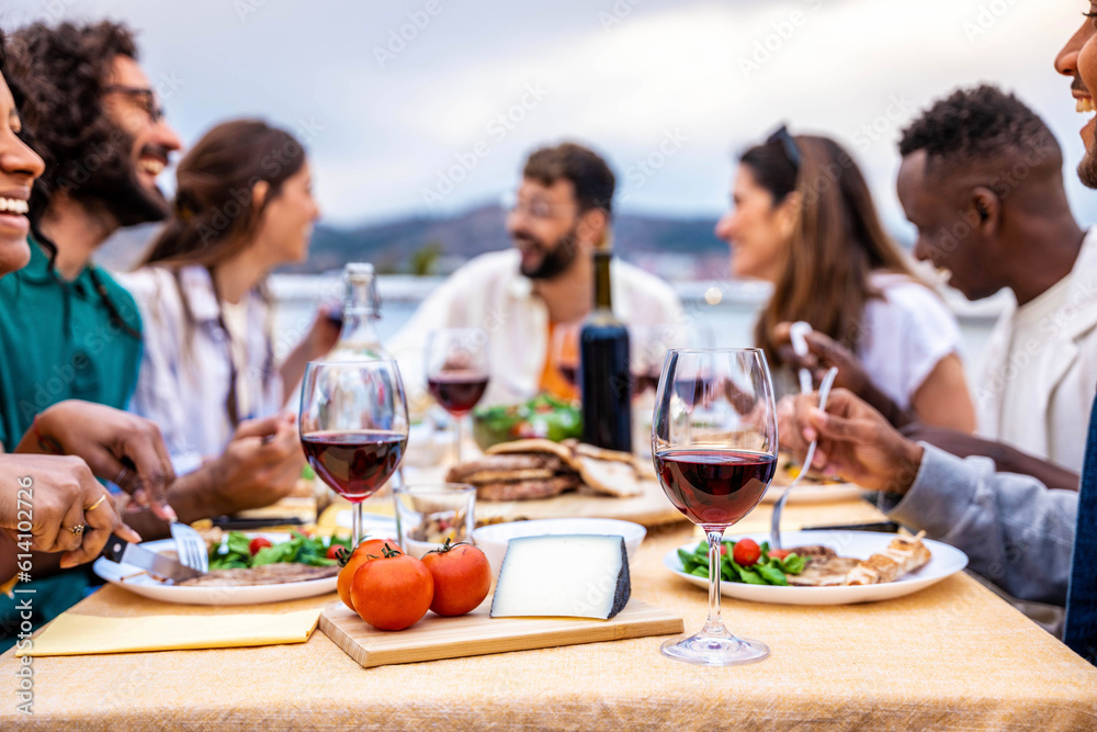 Young people enjoying delicious barbecue dinner party drinking red wine - Multiracial family having diner time together outside - Happy friends eating fresh food sitting at restaurant table Young people enjoying delicious barbecue dinner party drinking red wine - Multiracial family having diner time together outside - Happy friends eating fresh food sitting at restaurant table