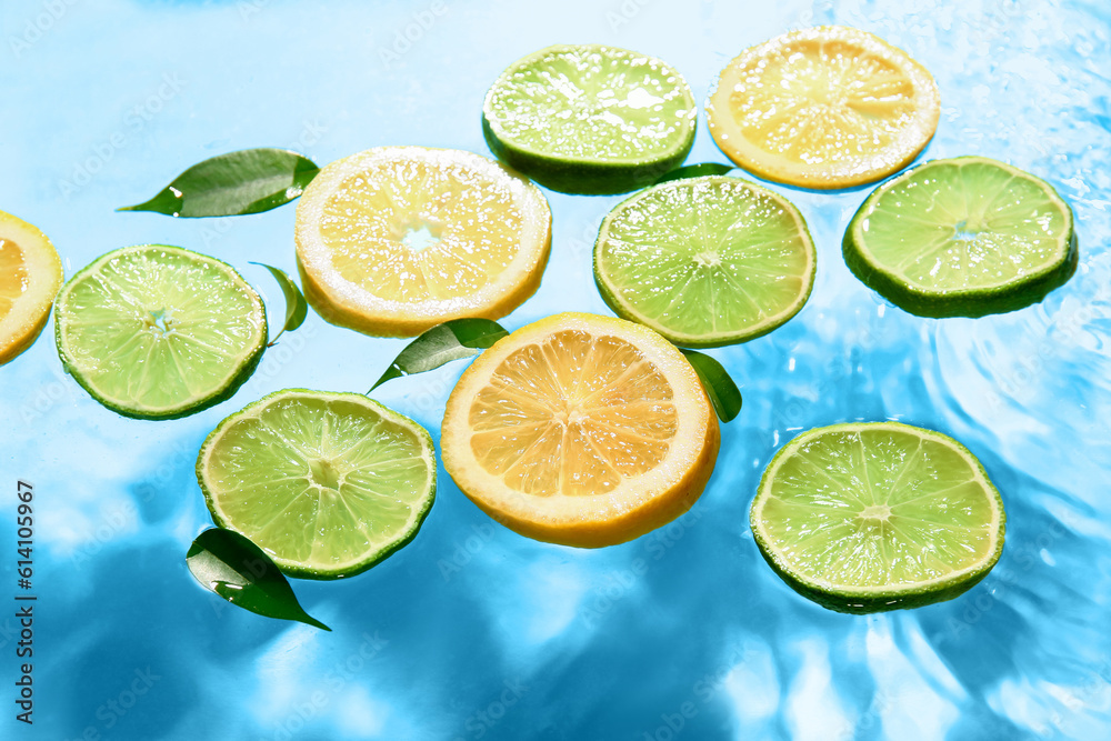 Slices of fresh lemon and lime in water on blue background