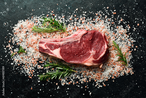 raw cowboy steak with salt on a stone background, first class rib on the bone. On a black stone table. Top view. photo