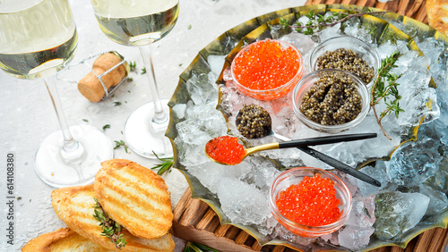 A set of black and red caviar in glass bowls on a metal tray with ice. On concrete texture background. Top view. Rustic style.