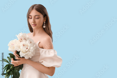 Beautiful young woman with bouquet of peony flowers on blue background