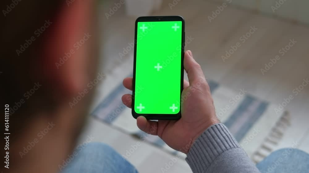Young man holding smartphone green mock-up screen in hand. Male person using chroma key mobile phone. Vertical mode. Touching, swiping display, tapping, surfing Internet social media. Gesturing Young man holding smartphone green mock-up screen in hand. Male person using chroma key mobile phone. Vertical mode. Touching, swiping display, tapping, surfing Internet social media. Gesturing