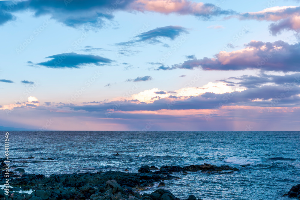 Naklejka premium amazing evening or morning sea shore landscape of blue water, rock coast and unique natural phenomenon of glow from below the sea to amazing sunset colorful clouds