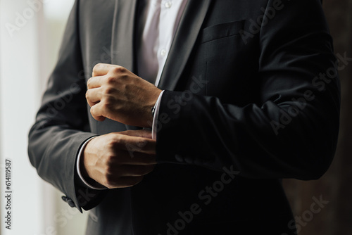 Obraz na płótnie Grooms morning preparation. Cropped photo of elegant young fashion man dressing up for wedding celebration. Groom dressed in modern black formal suit and white shirt, he getting ready for event. w salonie