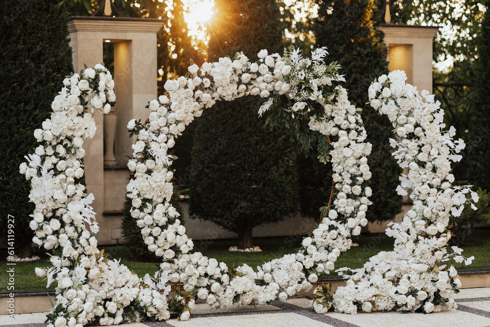 Round wedding arch with white flowers and greenery at sunset. The arch is decorated with flowers. Wedding decor.