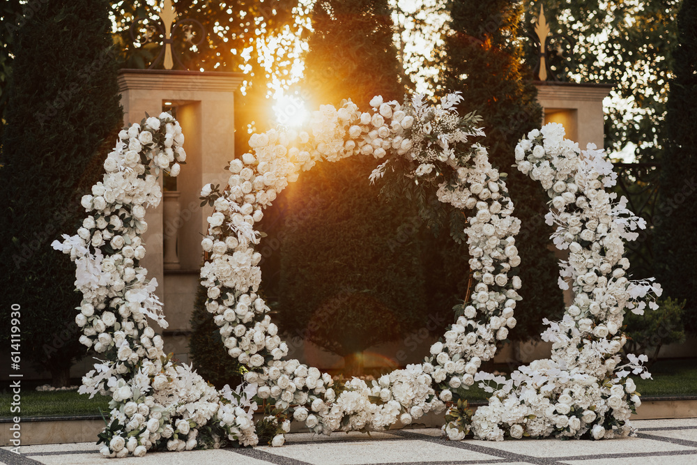 Wedding ceremony outdoor. Arch, decorated with white flowers standing in the garden, in the wedding ceremony area. Arch for the wedding ceremony at sunset.
