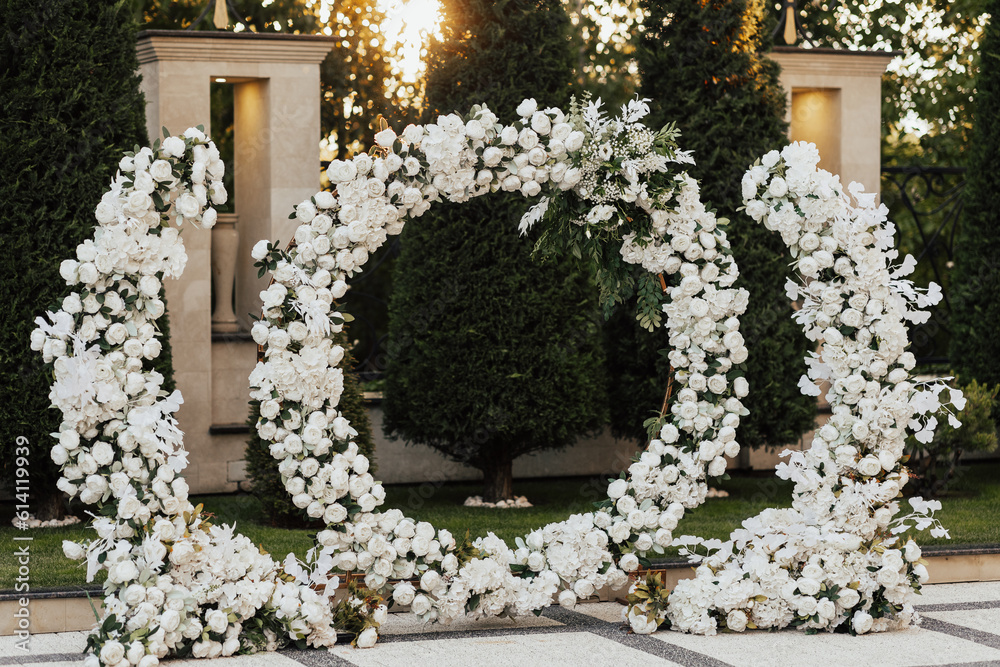 Wedding ceremony outdoor. Arch, decorated with white flowers standing in the garden, in the wedding ceremony area. Arch for the wedding ceremony at sunset.