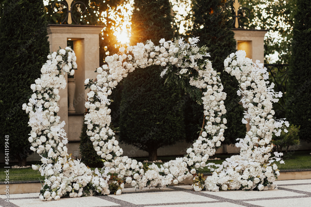 Wedding ceremony outdoor. Arch, decorated with white flowers standing in the garden, in the wedding ceremony area. Arch for the wedding ceremony at sunset.