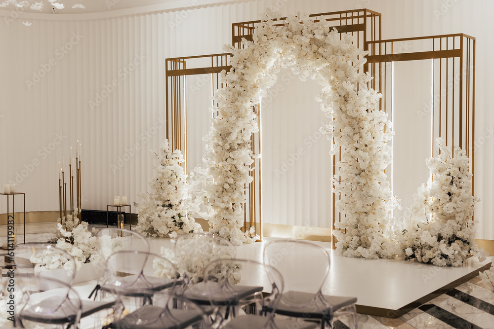 Wedding arch decorated by white flowers standing in the center of wedding ceremony in the luxury restaurant.