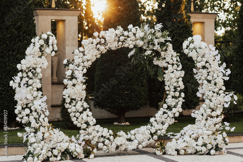 Obraz na płótnie Round wedding arch with white flowers and greenery at sunset. The arch is decorated with flowers. Wedding decor. w salonie