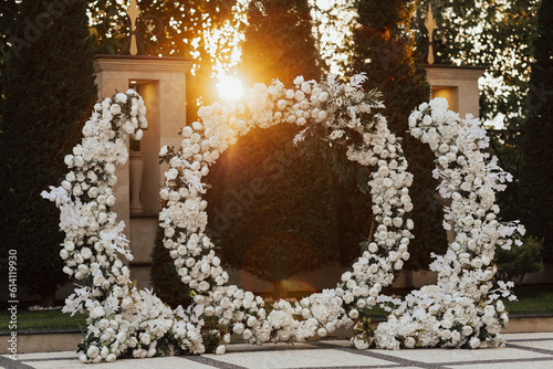 Wedding ceremony outdoor. Arch, decorated with white flowers standing in the garden, in the wedding ceremony area. Arch for the wedding ceremony at sunset.	